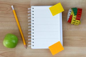 A blank notebook, green apple, pencil, measuring tape on wooden