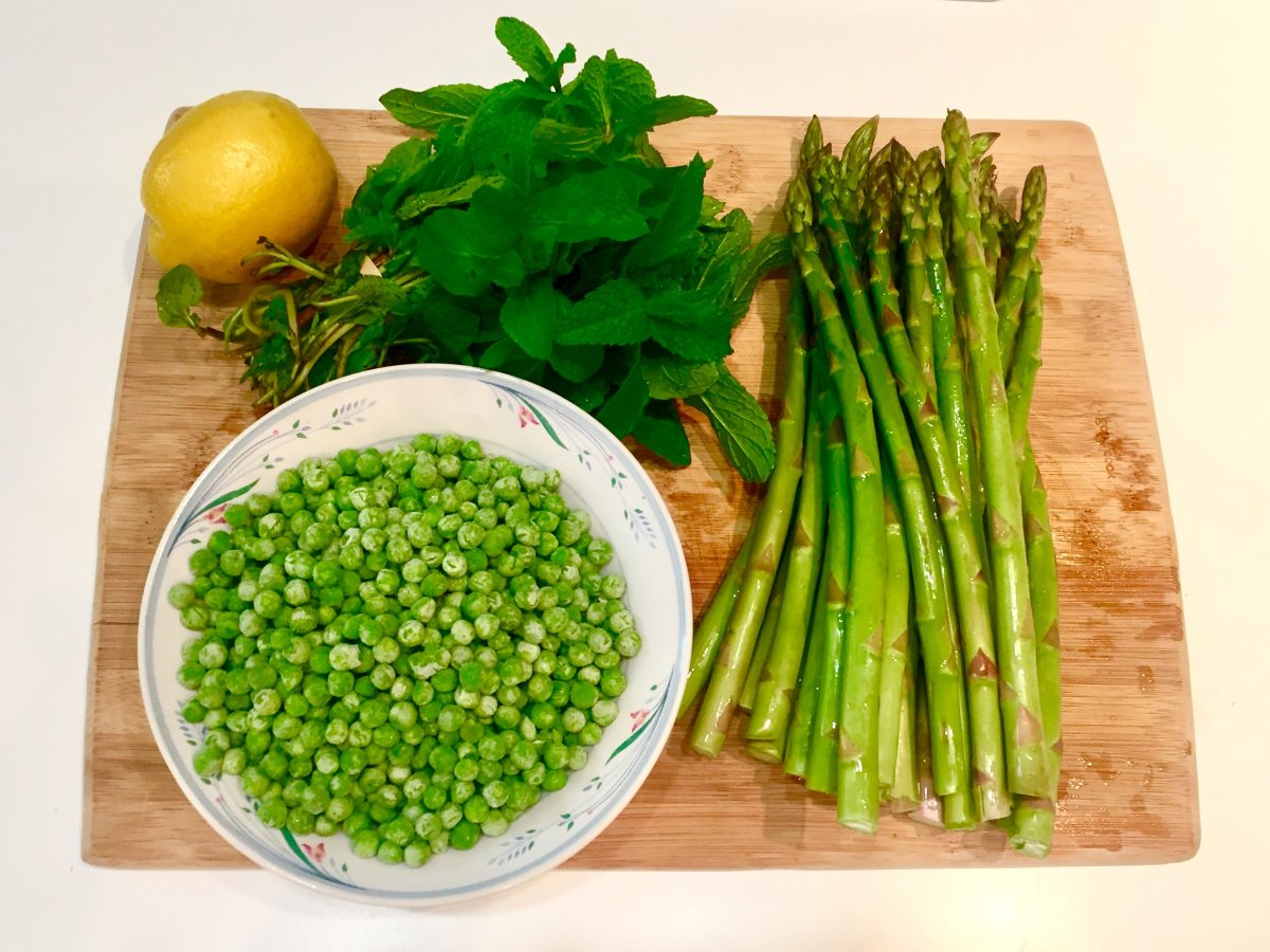 peas, asparagus, parsley, and an onion on a cutting board